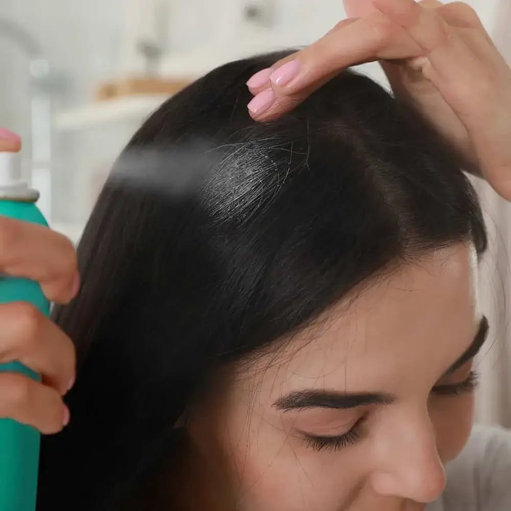 Close-up of a dry shampoo bottle being sprayed onto dark hair