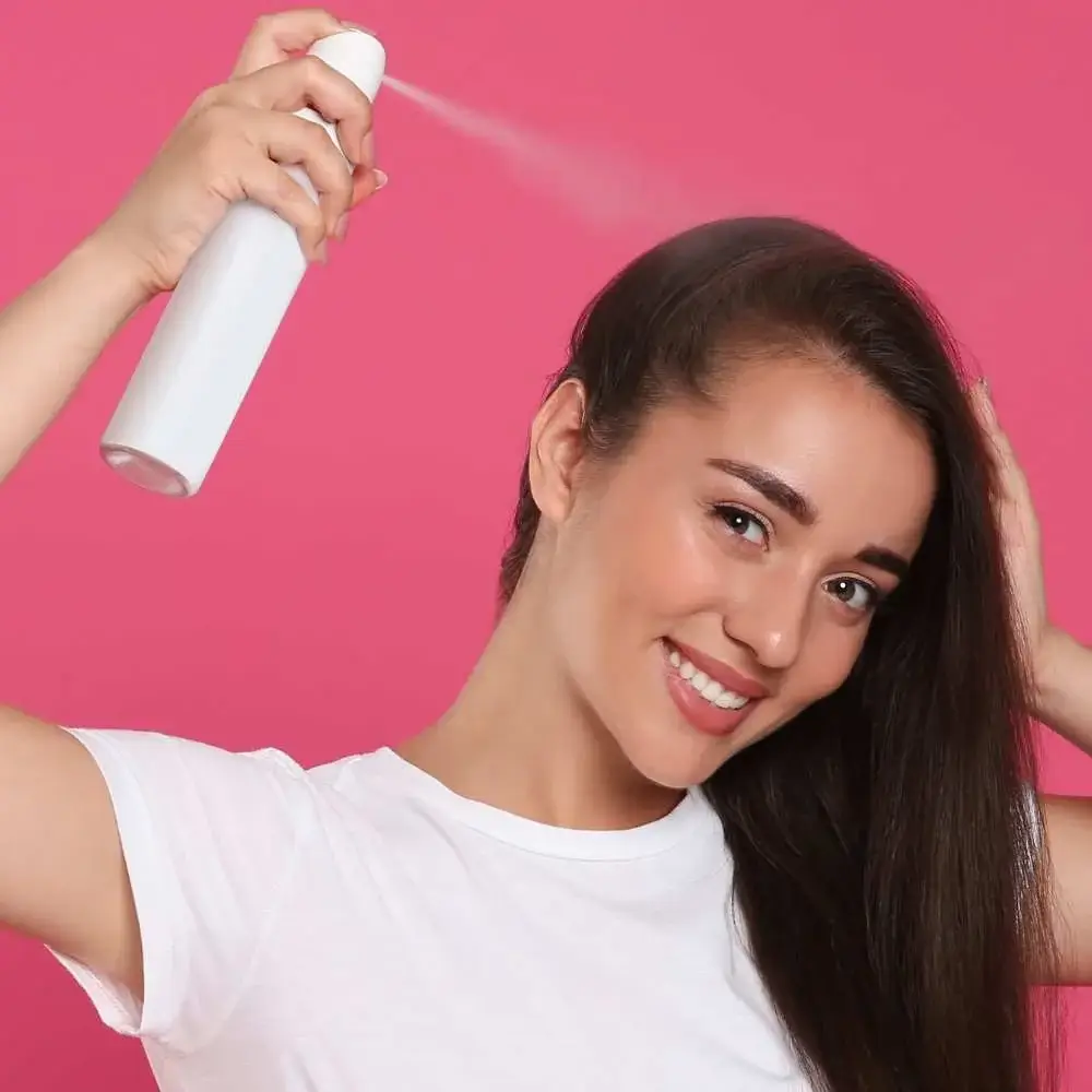 Hand spraying dry shampoo onto dark roots, demonstrating the application process