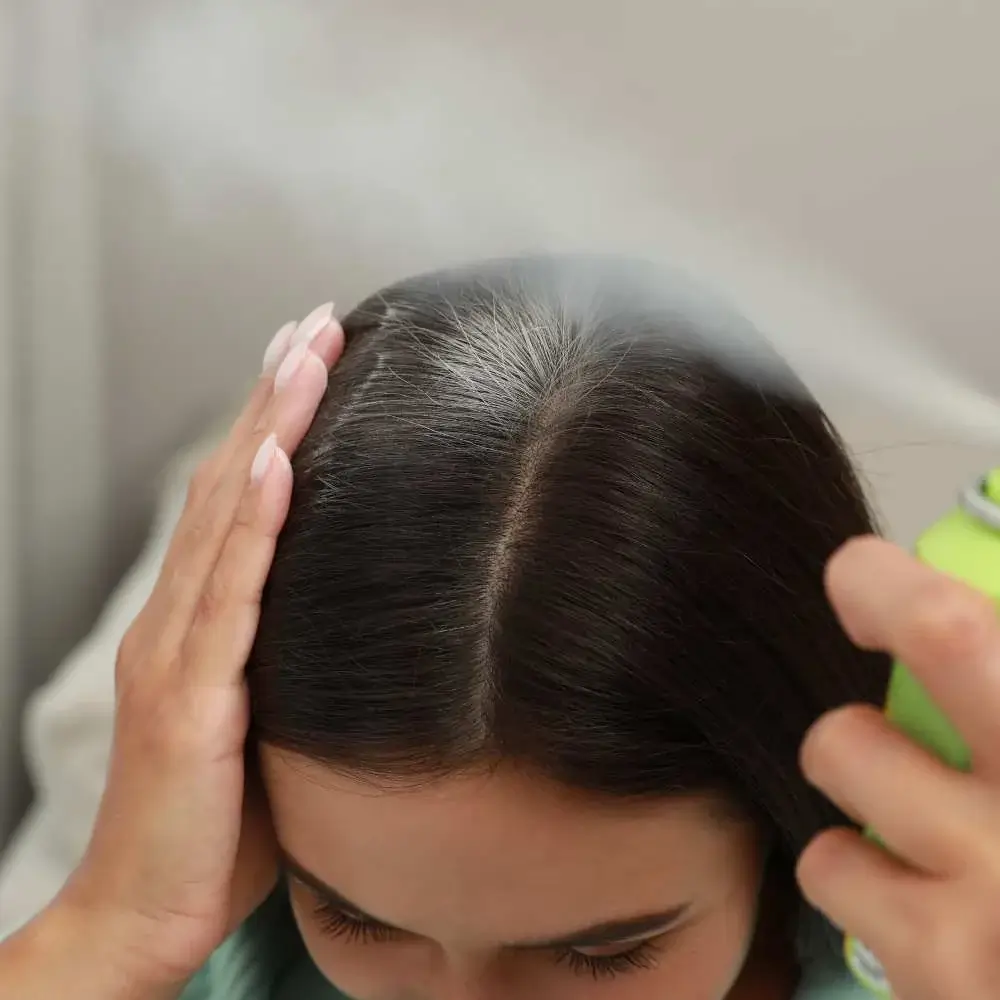 Woman with dark hair spraying dry shampoo to refresh her tresses