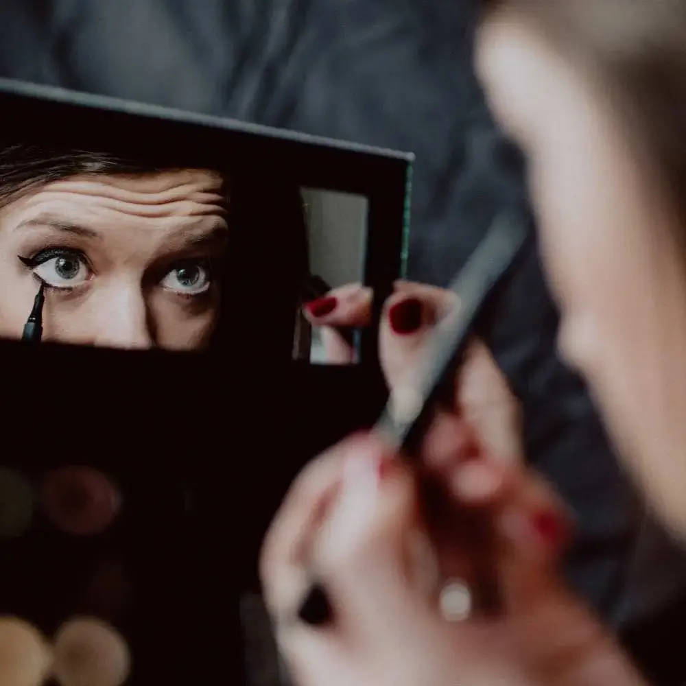Woman looking into a mirror while applying gel eyeliner for a night out