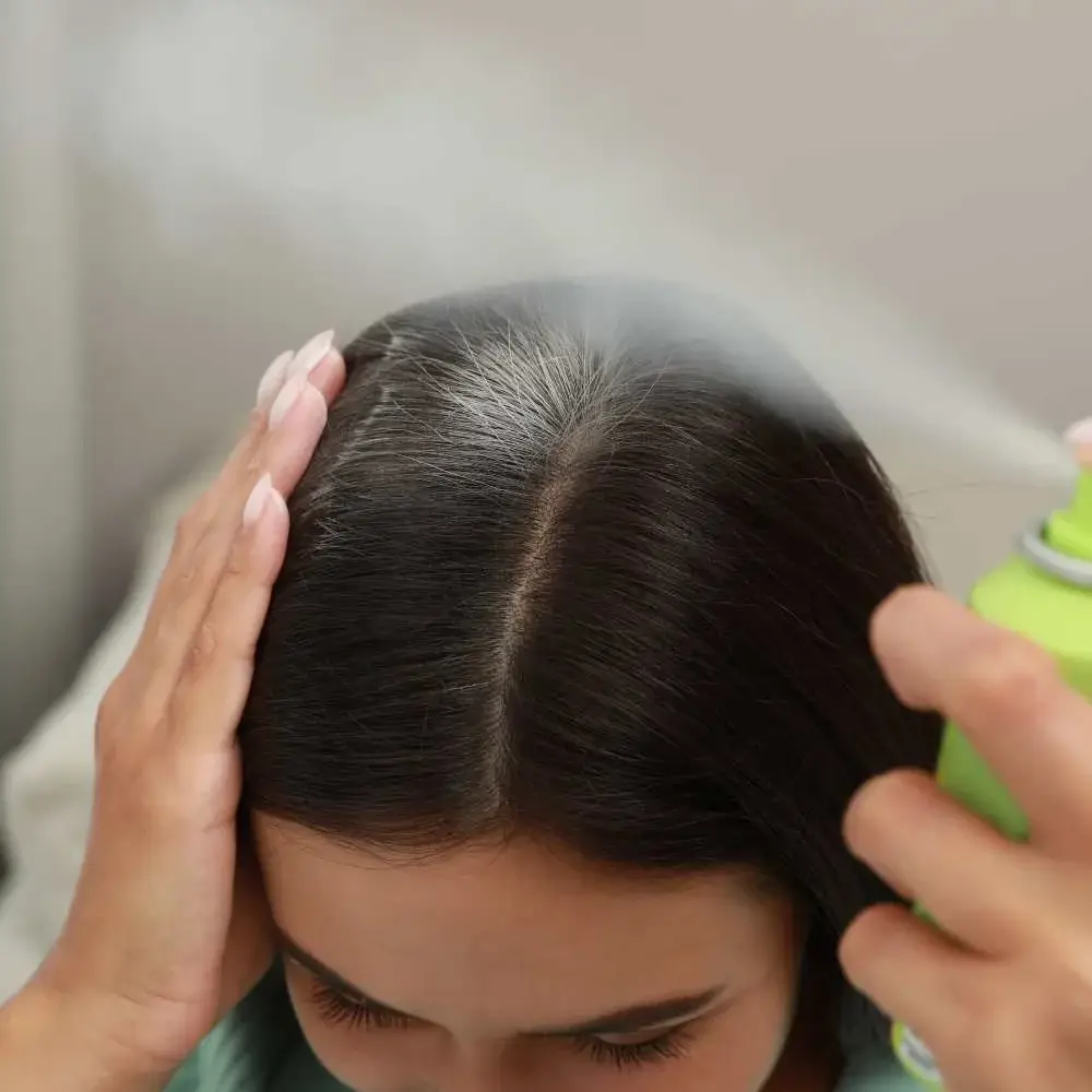 Close-up of a woman spraying dry shampoo into her hair