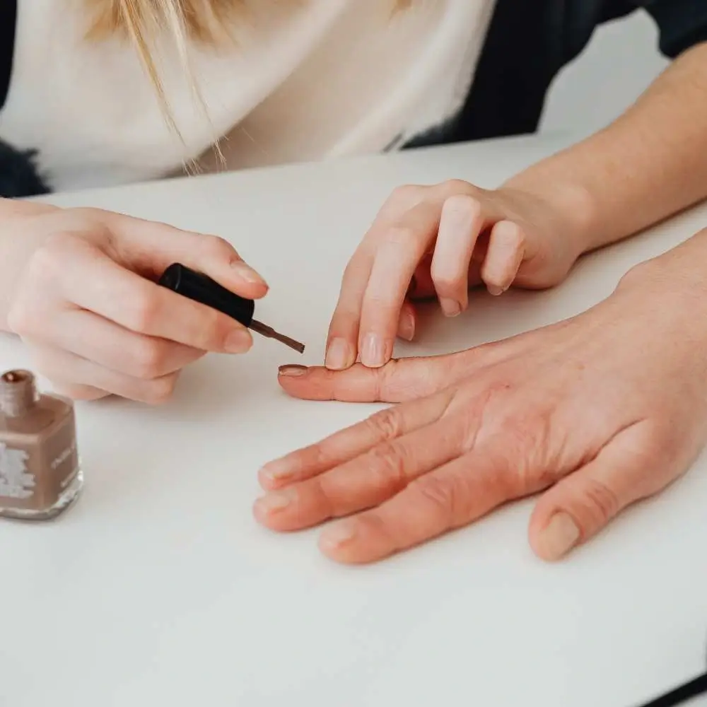 Woman applying nude nail polish, creating an elegant, minimalist look