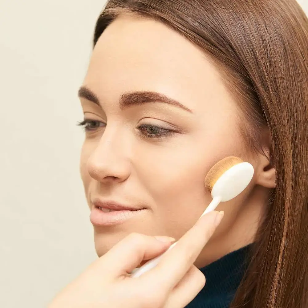 closeup portrait of a woman applying bronzer on her cheek