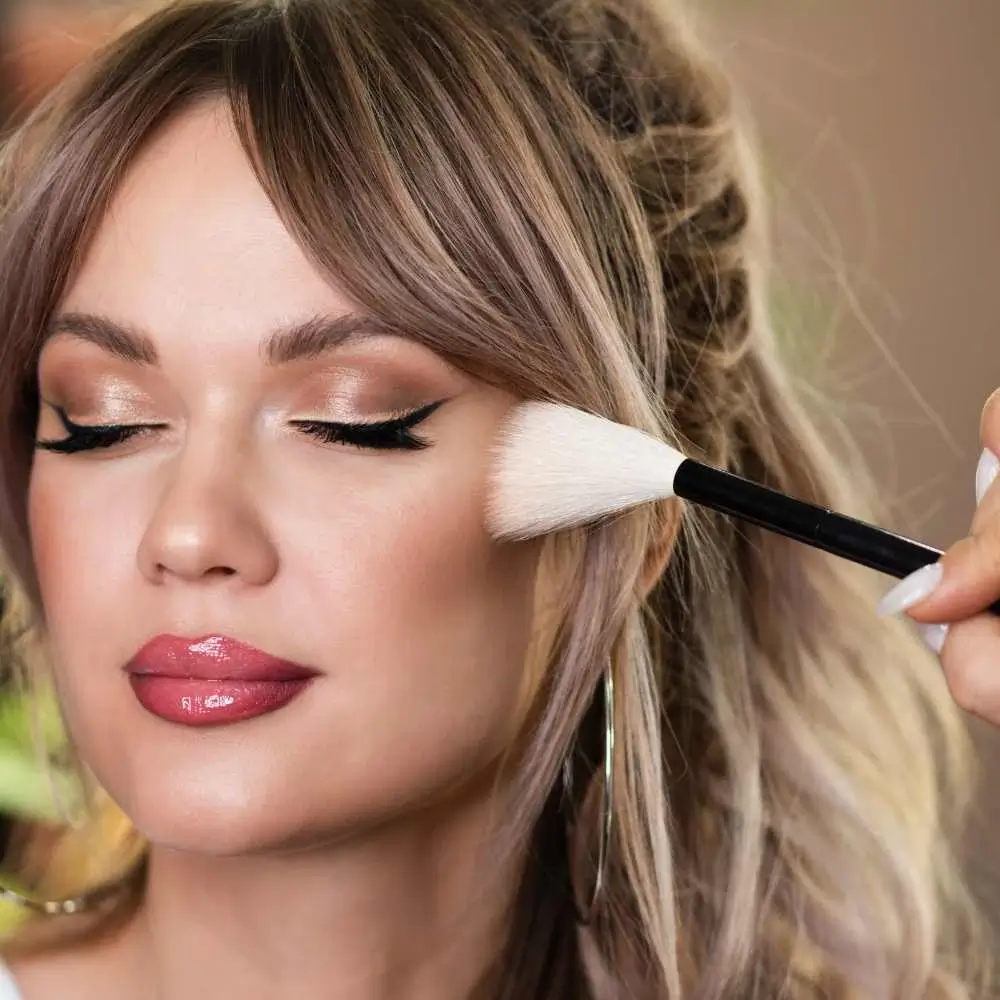 closeup portrait of a woman with makeup applying bronzer with a makeup brush