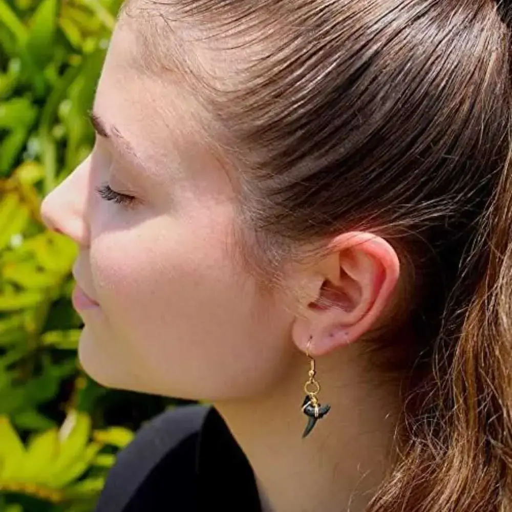 side view portrait of a young woman wearing black shark tooth earring