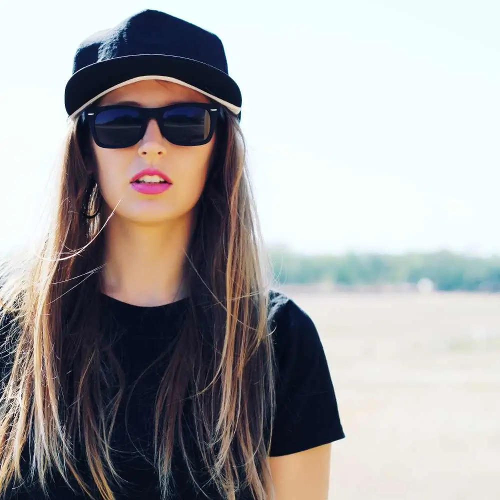 young woman with straight hair wearing a cap and sunglasses