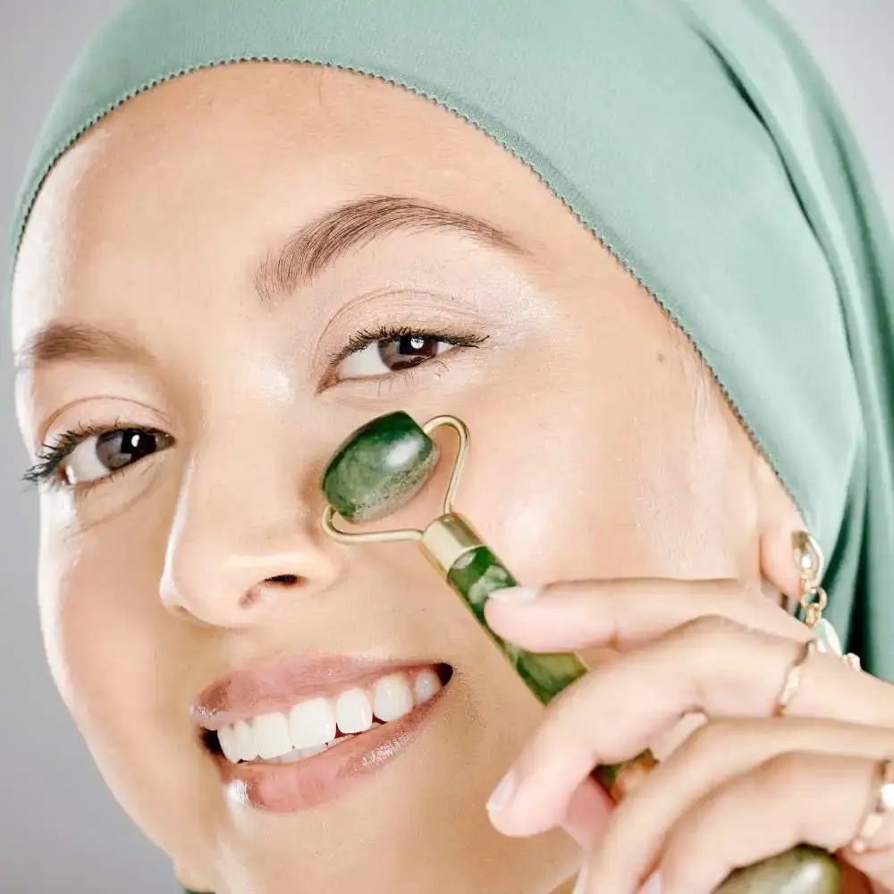 close up of a smiling woman's face while holding a jade face roller against her cheek