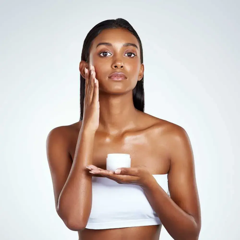 young woman holding a face moisturizer while touching her face