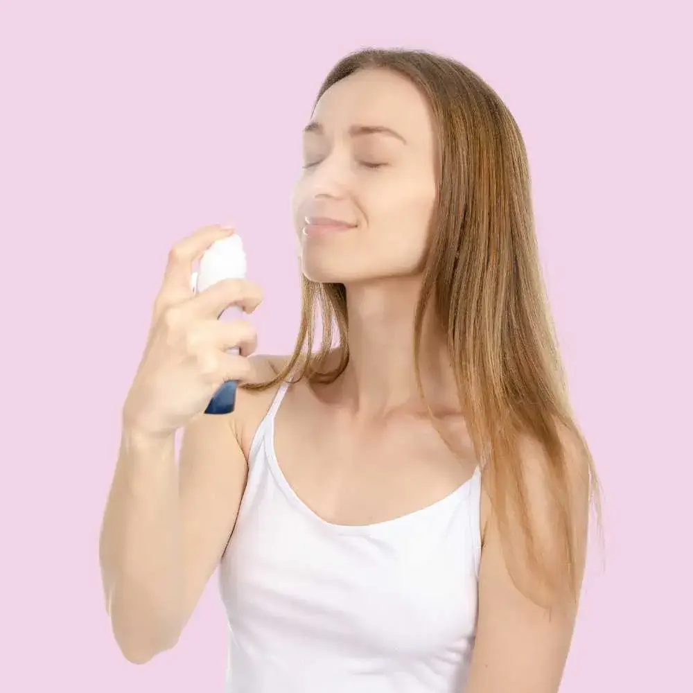 blonde young woman spraying her face with makeup setting spray