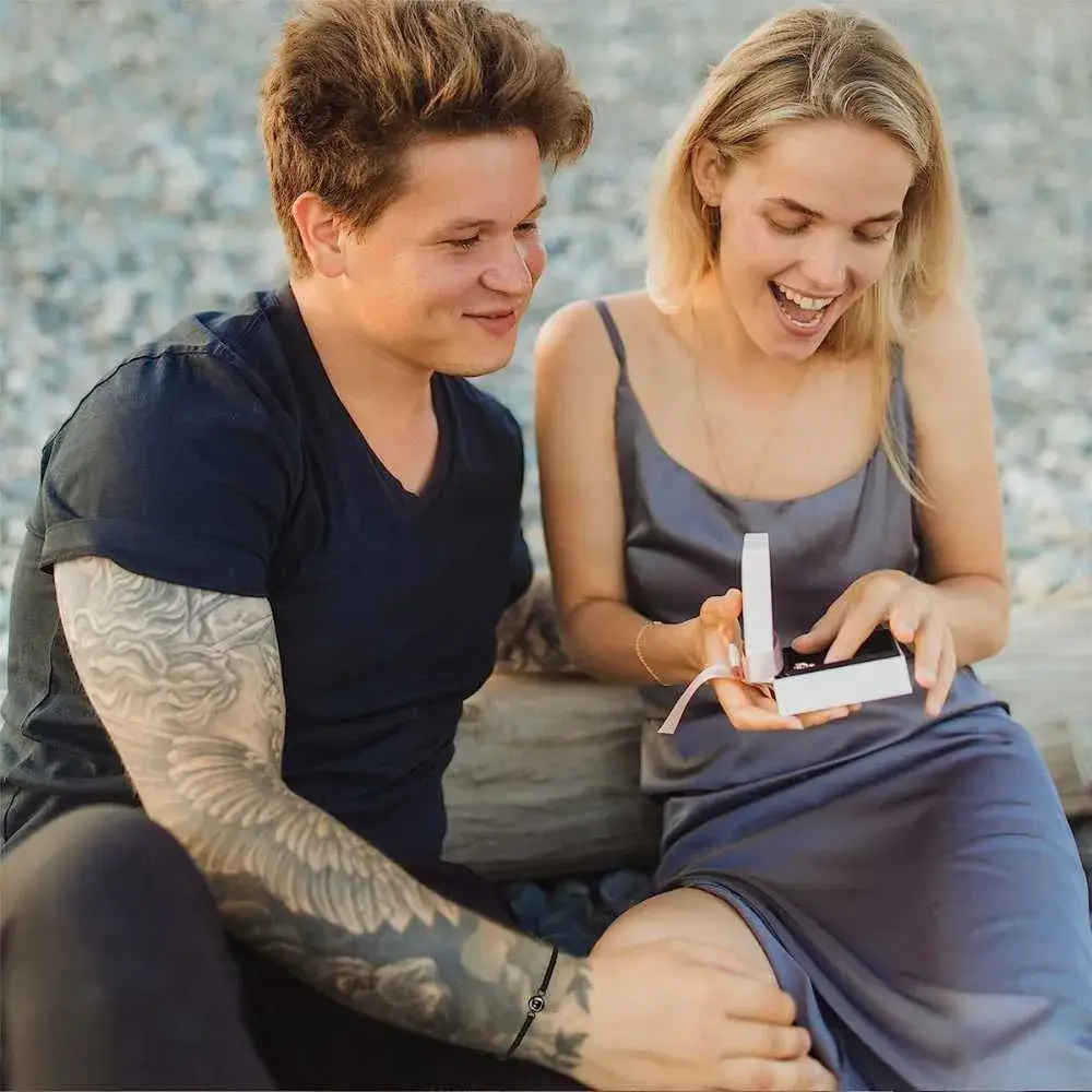 young man with tattoo and a young woman opening a present with a big smile