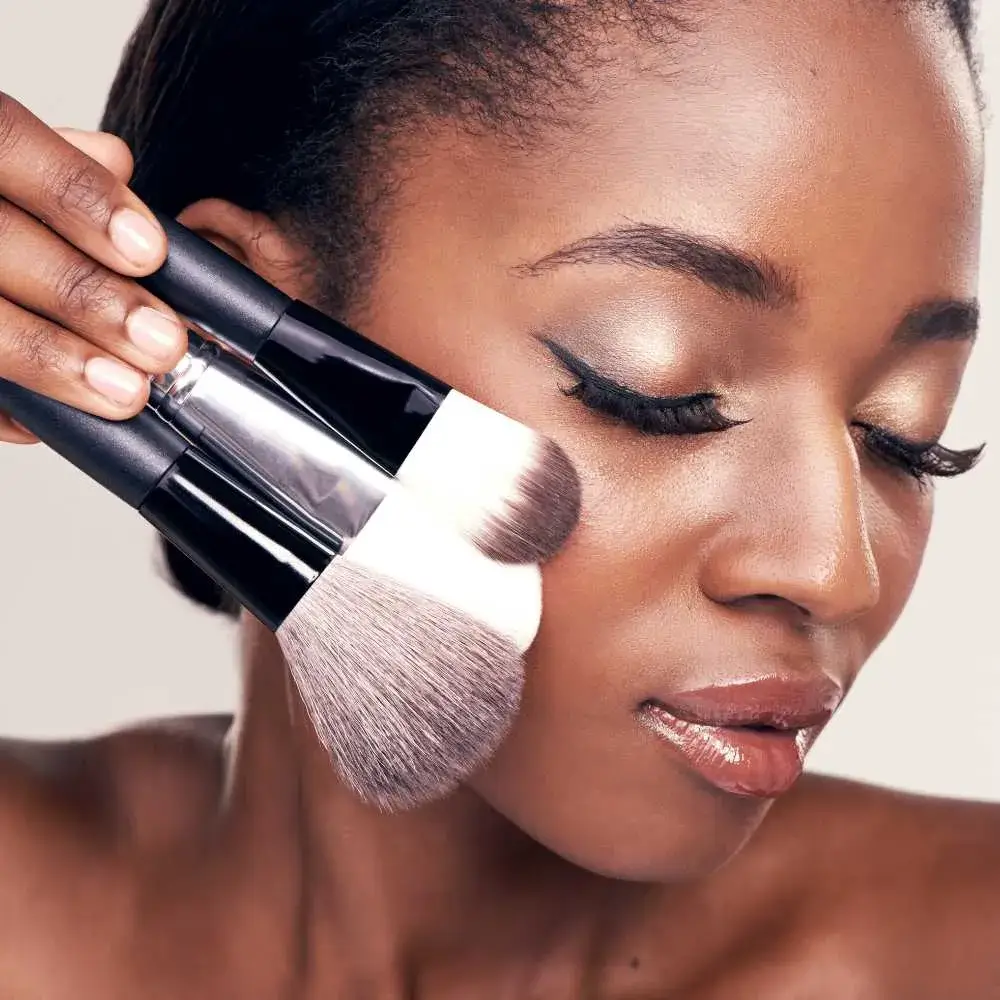 closeup portrait of a black woman holding makeup brushes against her cheek