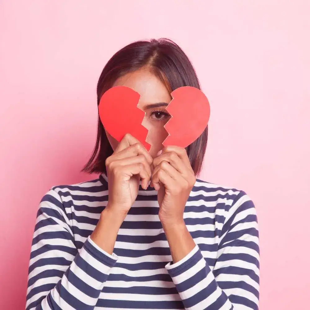 woman with short hair and wearing stripes holding a broken heart against her face