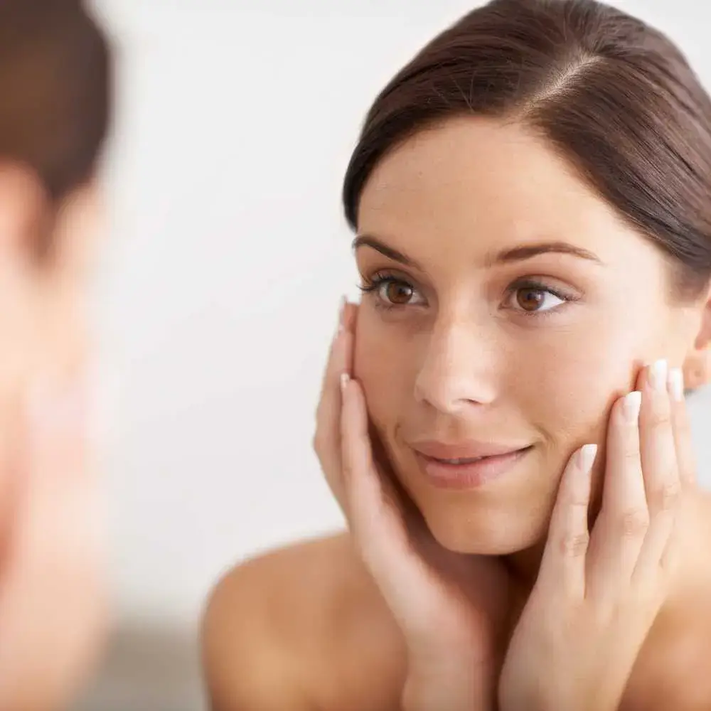 closeup of a brunette young woman looking at her face in the mirror