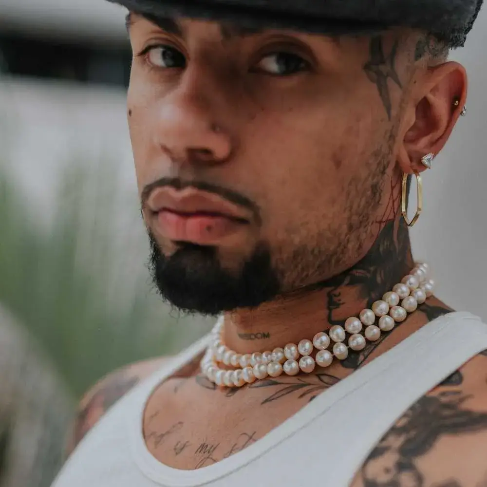 man with tattoos wearing pearl necklace