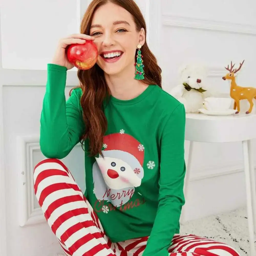 Brunette with christmas tree earring smiling and holding an apple in her green sweater 