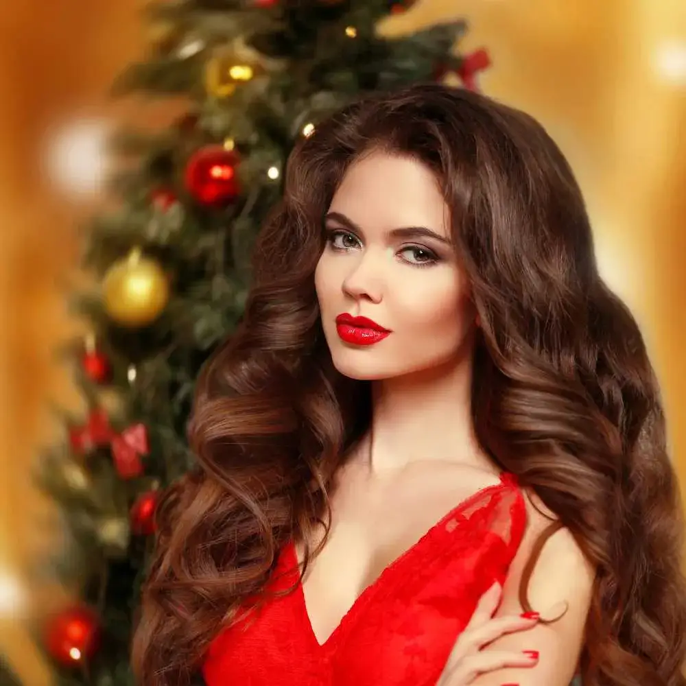 portrait of gorgeous young woman with makeup in red dress with christmas tree in the background