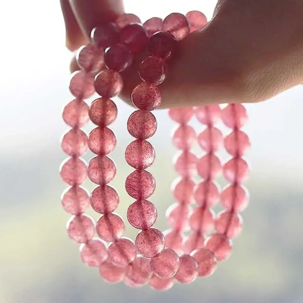 close-up view of a hand holding three strawberry quartz bracelets