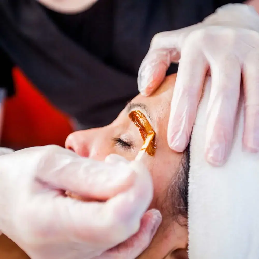 Professional aesthetician preparing to wax a client's right eyebrow