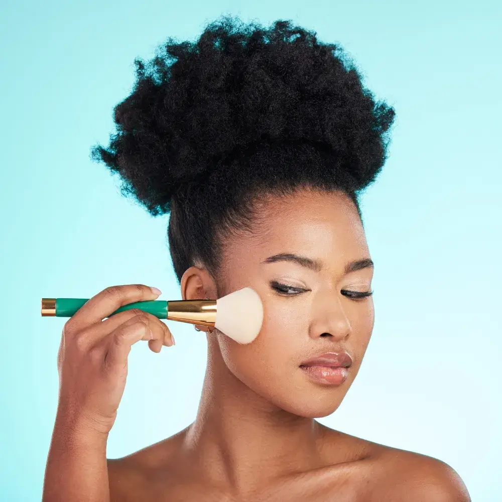 woman with curly hair holding a makeup brush against her cheek