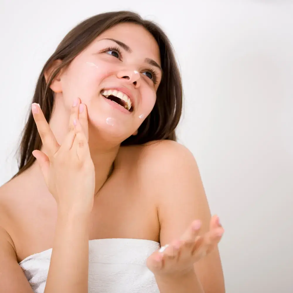 happy woman putting moisturizer on her face