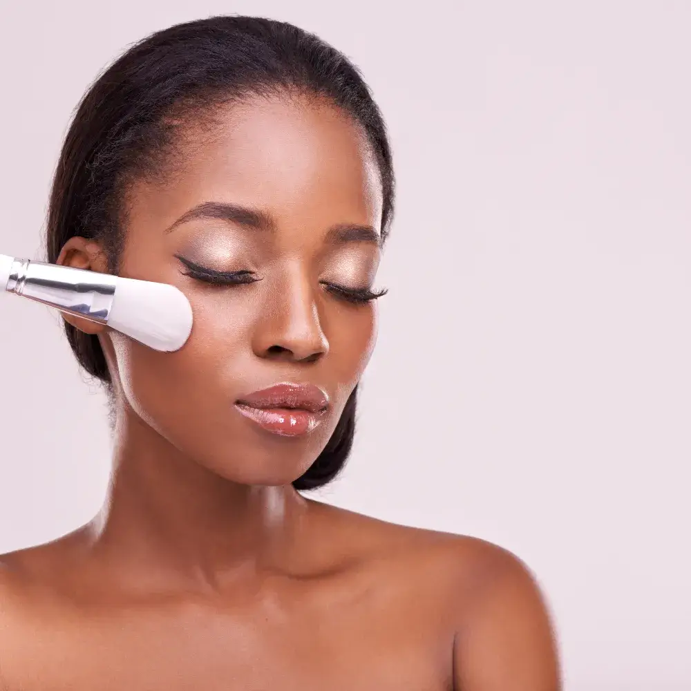 black woman applying powder foundation on her cheek