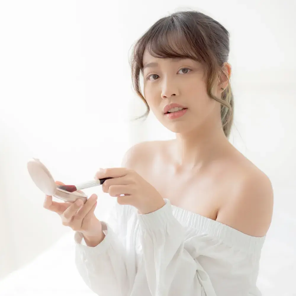 asian young woman holding a makeup brush and compact powder
