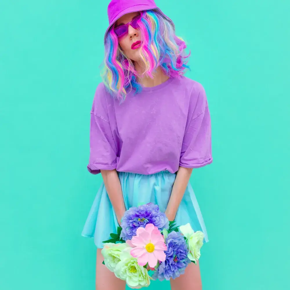 young woman wearing colorful outfit with rainbow-colored wig and holding flowers with both hands