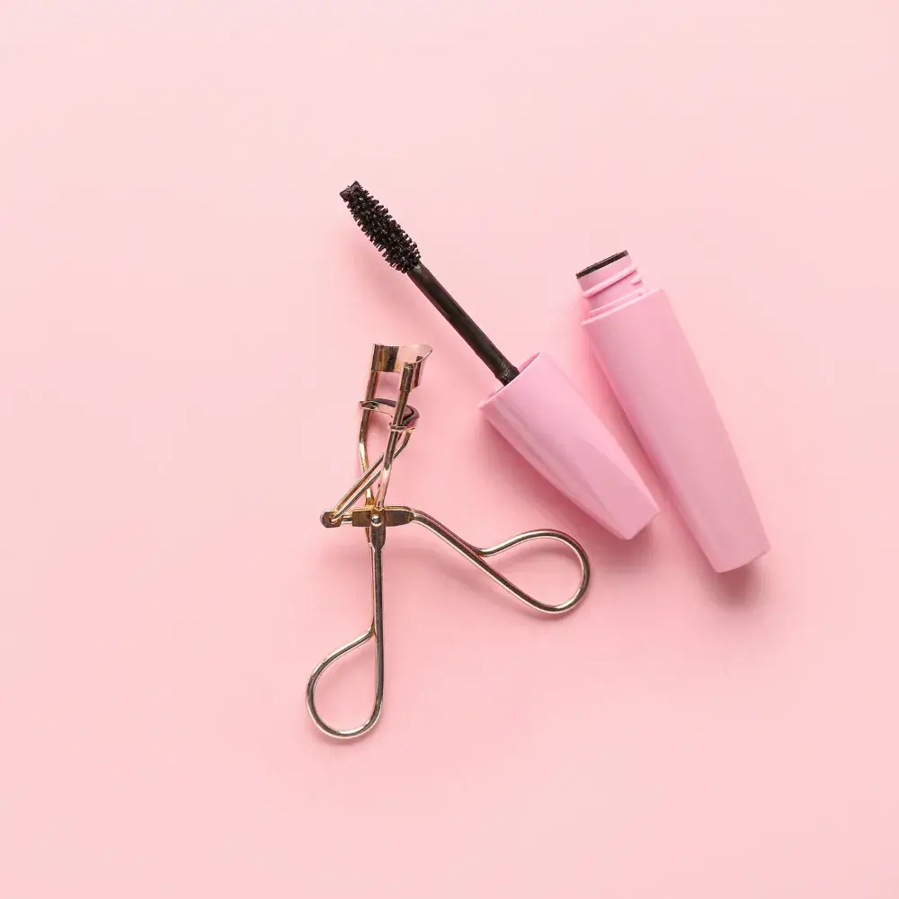 pink mascara and eyelash curler on a light pink background