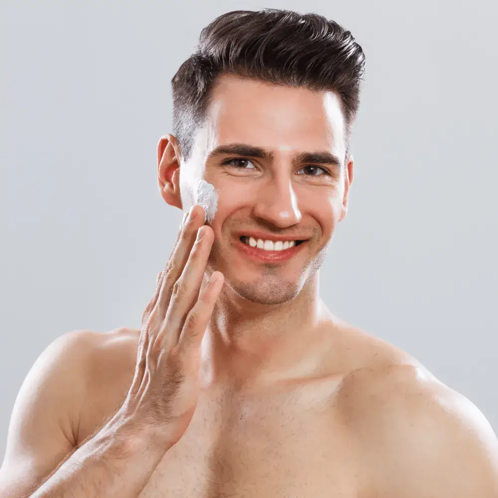 young man smiling while applying cream on his face