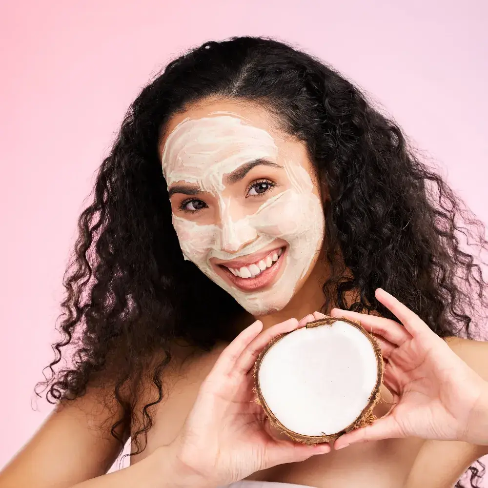 smiling curly haired woman with face mask and holding coconut