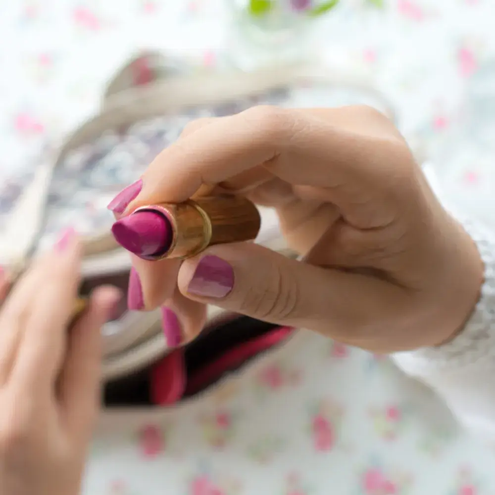 close up of a hand holding a dark pink lipstick