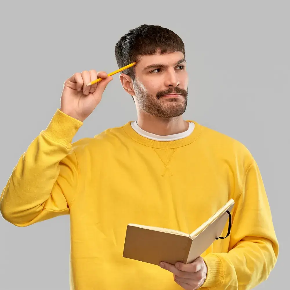 young man in a yellow sweatshirt holding a notebook and a pencil