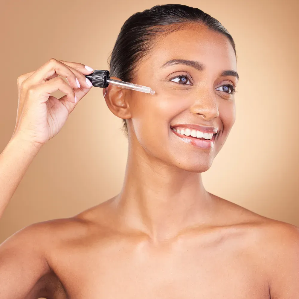 portrait of a young woman smiling while applying face oil on her face