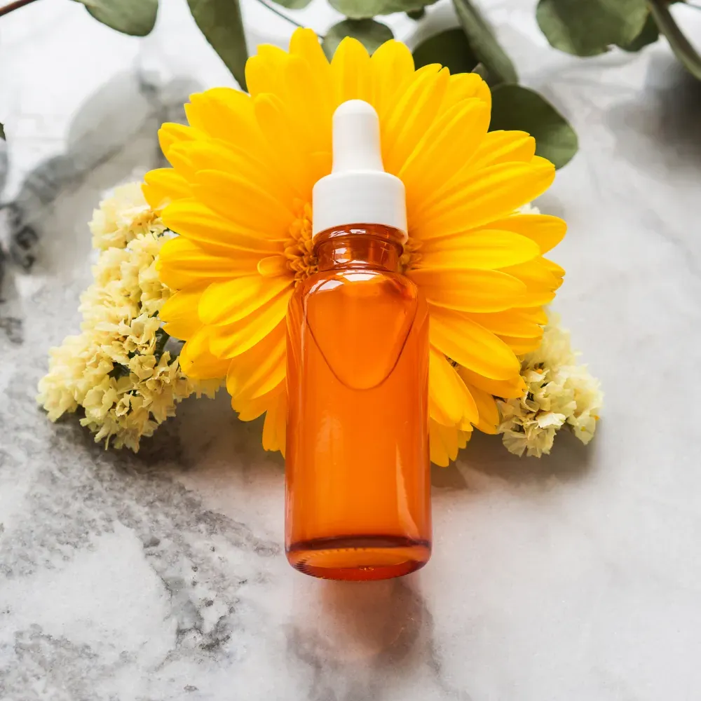 Face oil in an orange bottle, placed over yellow flowers