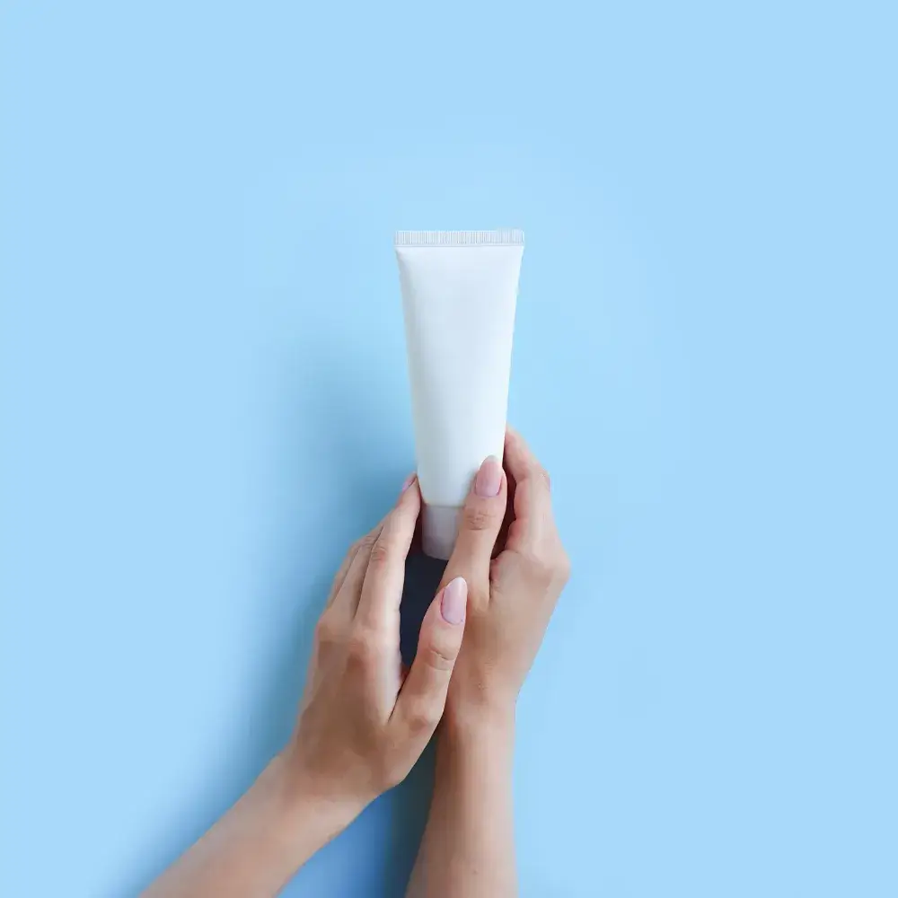 hands holding a white cosmetic tube against a light blue backround