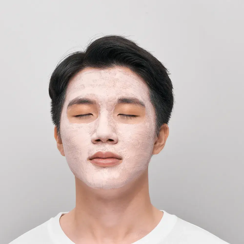 A young Asian man wearing a clay mask with his eyes closed