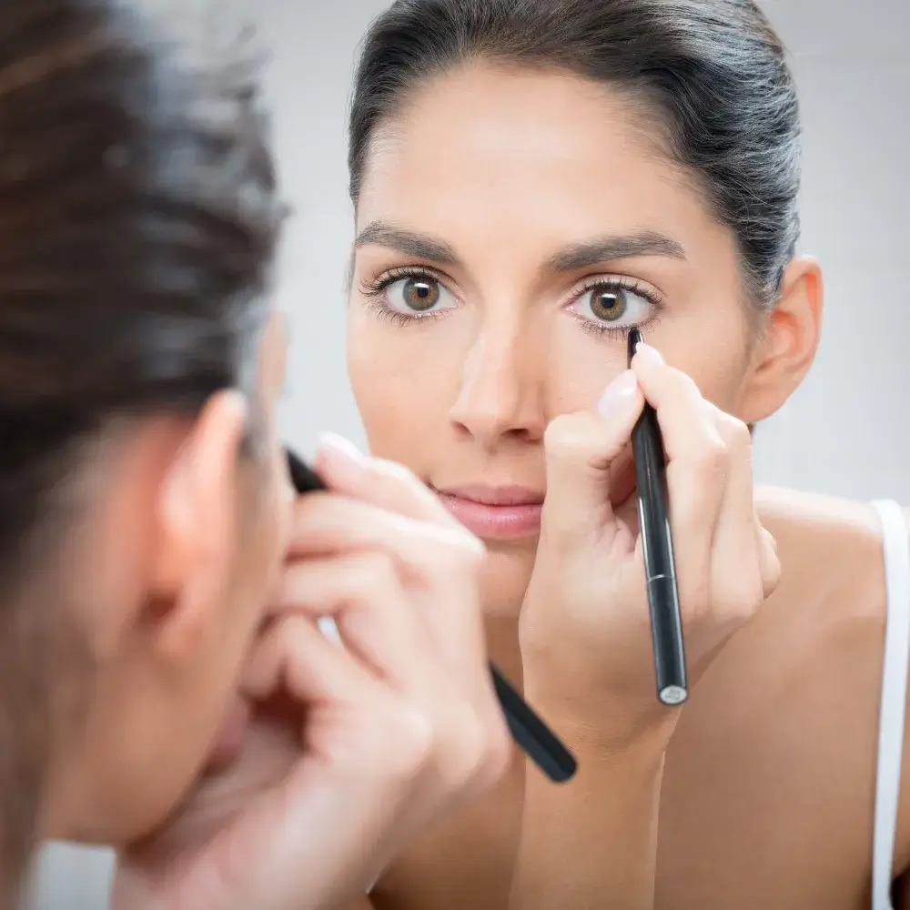 woman applying black eyeliner on her lower lash line in front of a mirror