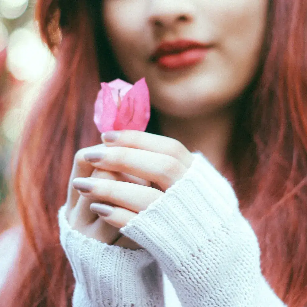 close up of a woman's hands with nail polish holding a pink flower