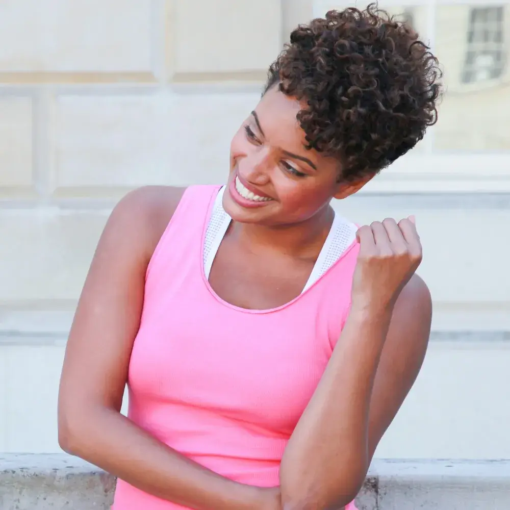 smiling black woman with curly hair wearing a pink top
