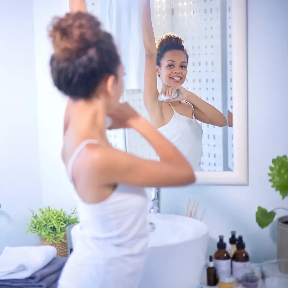woman wearing a white top and applying deodorant in front of the mirror