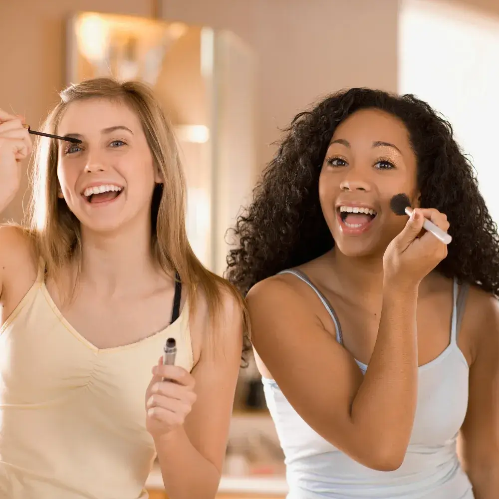 two women doing their makeup by applying mascara and blush