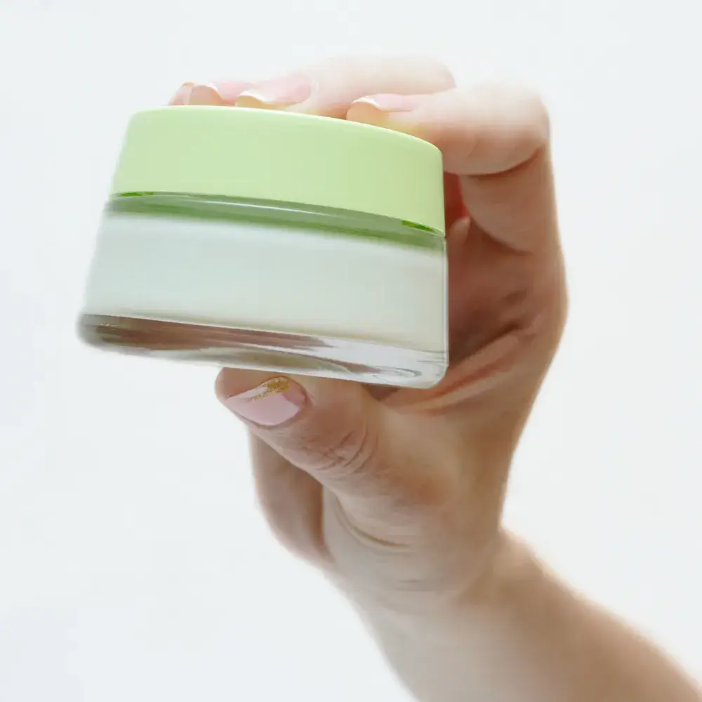 close-up of a hand holding a glass container of a hand cream