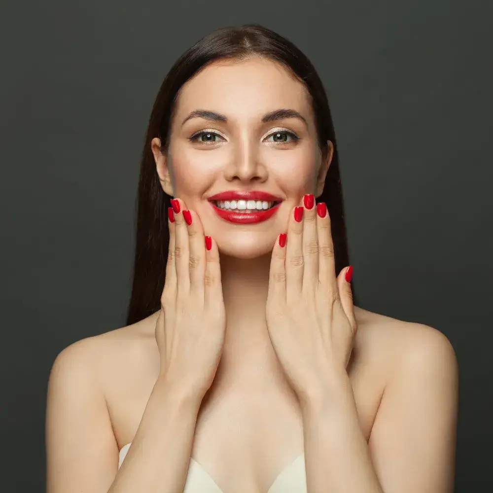 smiling woman wearing red lipstick and red nail polish with hands on her face