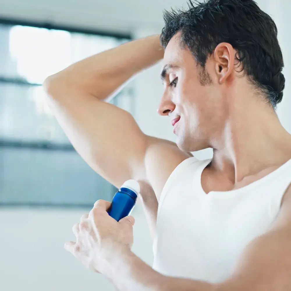 side view of a man in a white tank top applying deodorant on his underarm