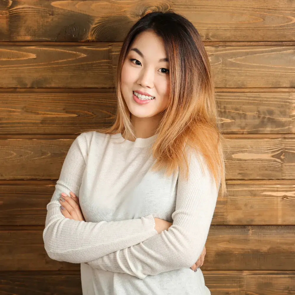 A young Asian woman with dyed hair is wearing a white sweater against a wooden background