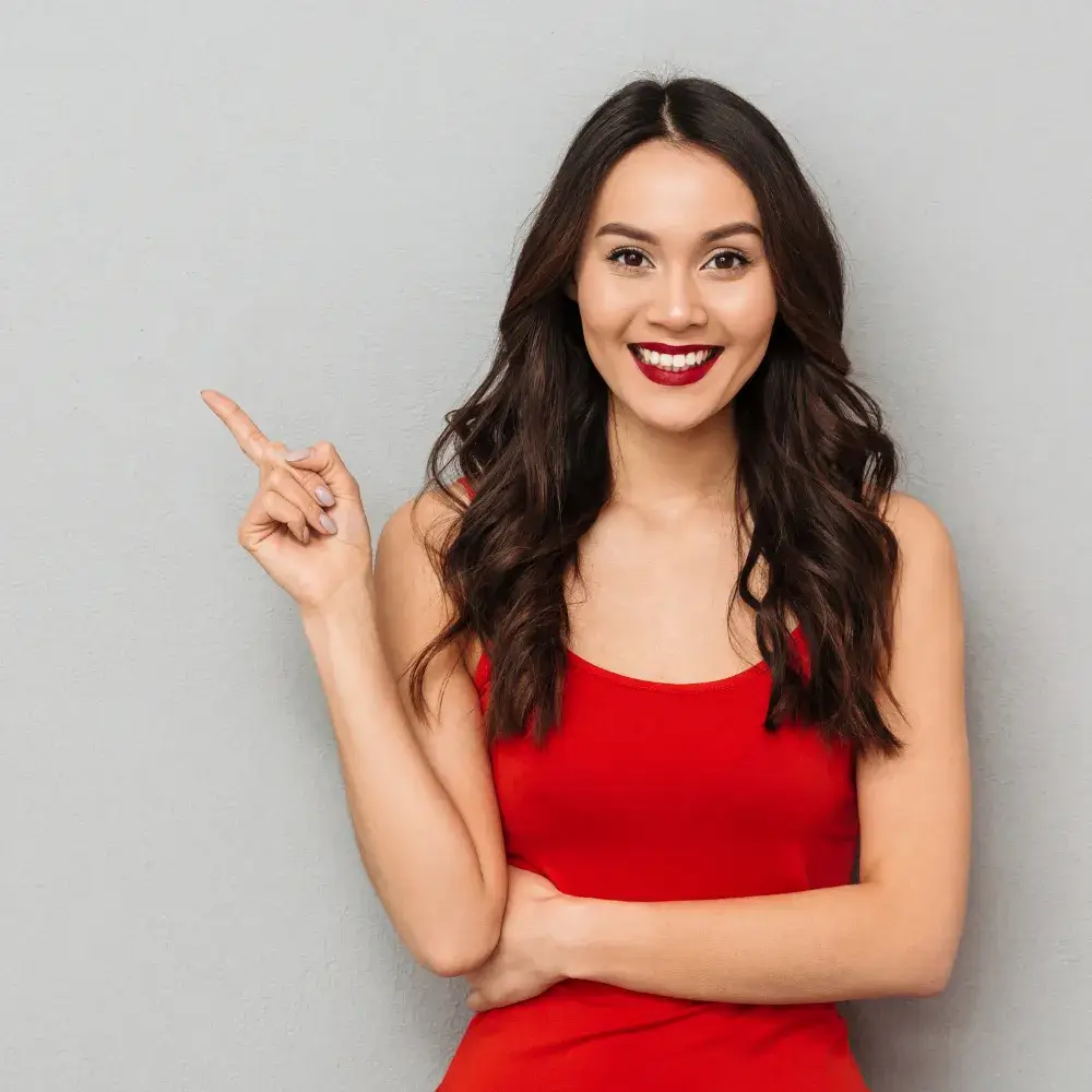 An Asian woman in a red top, wearing red lipstick and with curled hair, is posing against a grey background