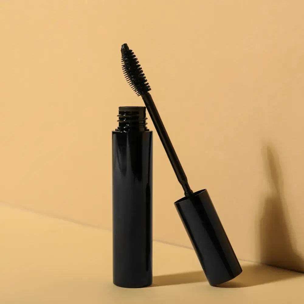 black mascara wand and bottle against a beige background