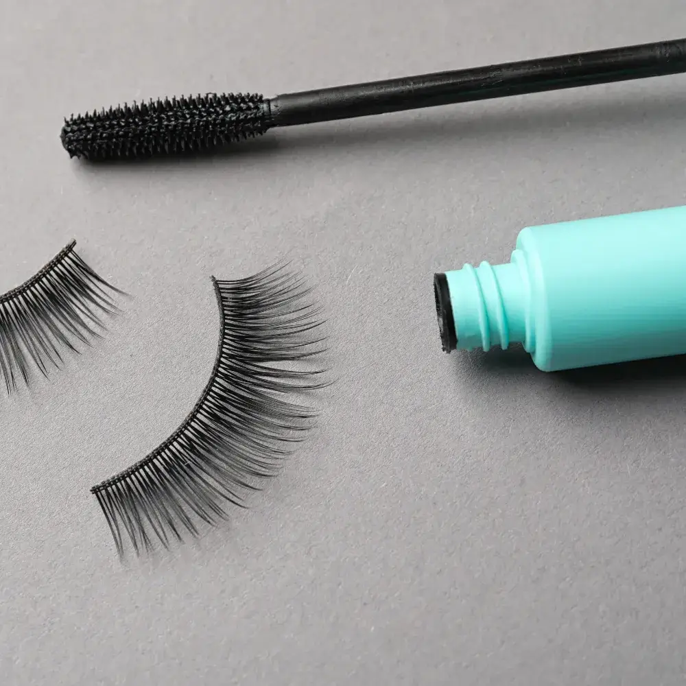 mascara and a pair of false eyelashes against a gray background
