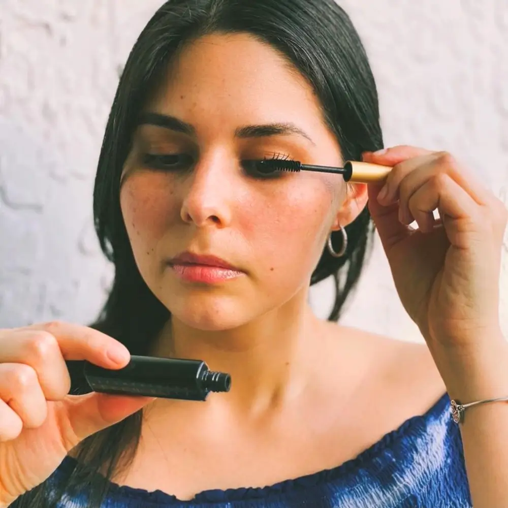 close up portrait of a woman in blue shirt applying black mascara