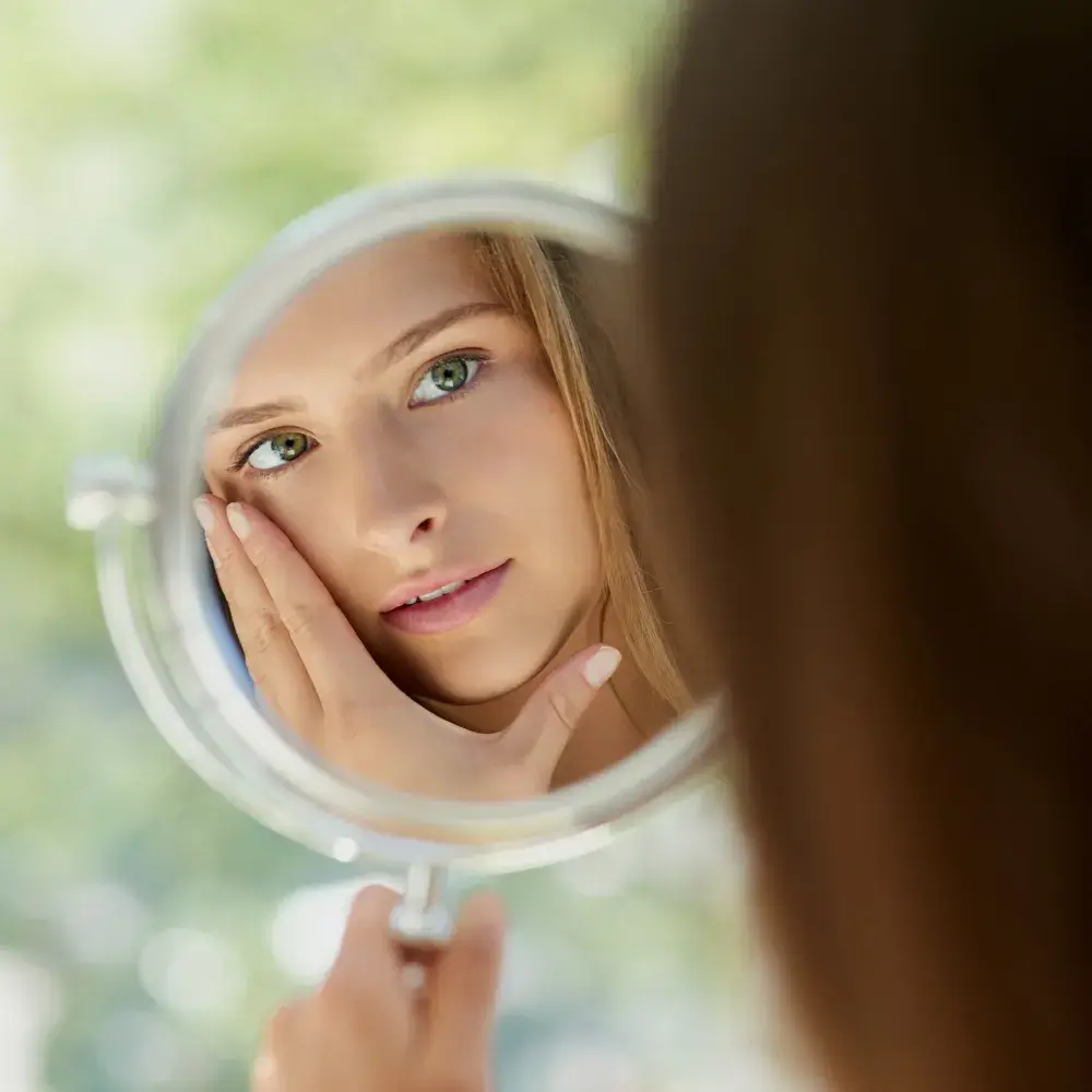 young woman looking at her face in the mirror